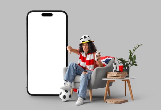 Displeased female African-American soccer watching game and big mobile phone with blank screen on grey background