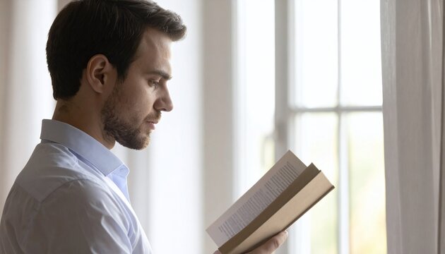 A calm man in a light blue shirt deep in a book near a bright window. It captures study, focus, and knowledge. Ideal for academic, personal growth, and mindfulness marketing projects.