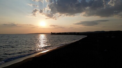 Obraz premium Europe, Italy, Rome - Santa Severa and the black volcanic beach with a castle on the horizon during a summer sunset - holiday near Santa Marinella on the Via Aurelia