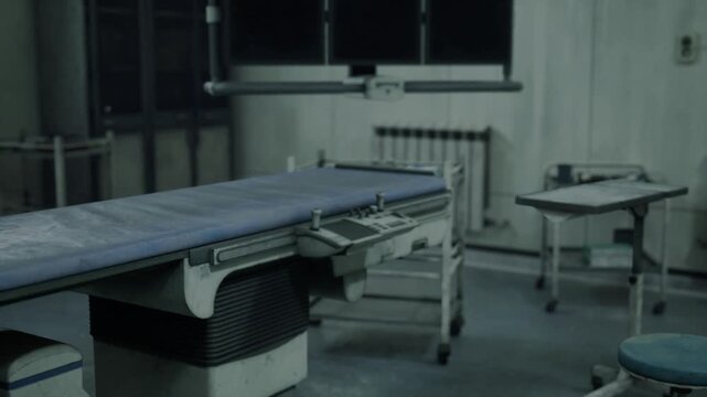 Abandoned operating table in dim room showing surgical instruments, sterile tray, overhead lamp, dust layers, neglected anesthesia tubing, clinical green