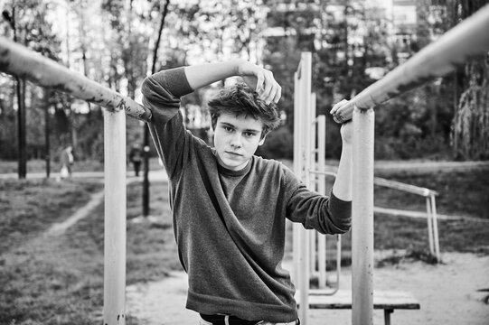 Teen boy posing between parallel bars in outdoor workout park, black and white portrait with calm confident expression. For youth lifestyle, fitness branding, wellness content, or editorial use.