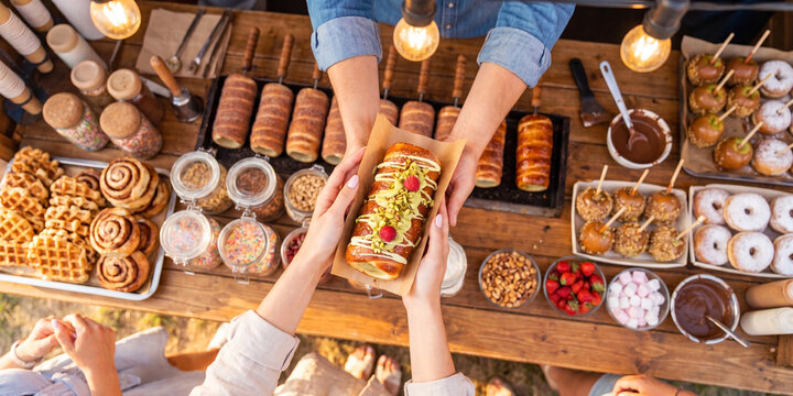 Top view of customers choosing chimney cake at market stall, traditional bakery selection concept.