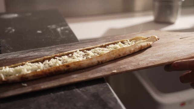 Professional chef preparing a traditional Turkish pide, sprinkling grated cheese on top before baking, fa01