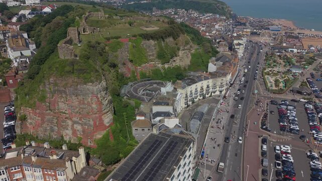 From Hastings to old fishing town aerial view. Forward motion above the road and amusement park to the Stade beach. Flying by the cliff with castle ruins and St. Mary church under the cliff.