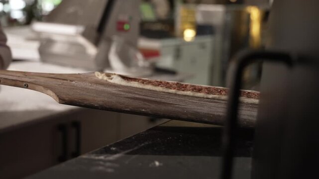 Baker's hands preparing a long dough with minced meat filling, placing it on a wooden peel, fa01