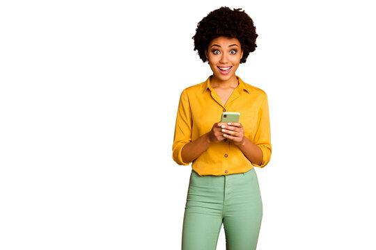 Photo of funny dark skin wavy lady holding telephone hands influencer open mouth read positive comments wear yellow shirt green trousers isolated brown color background