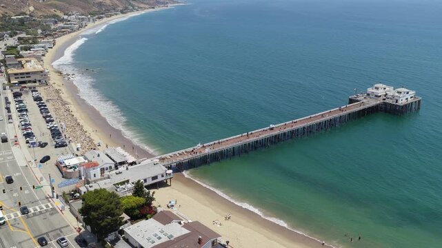 Malibu Pier and Surfrider Beach aerial showcasing coastal real estate and Pacific Coast Highway with gentle ocean waves on clear sunny Southern California day