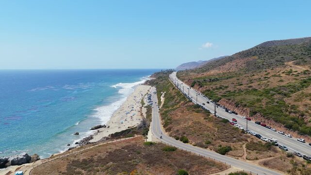 Sunny day traffic on Pacific Coast Highway with cars parked along Leo Carrillo State Beach in Malibu, California people relaxing on sand and ocean waves
