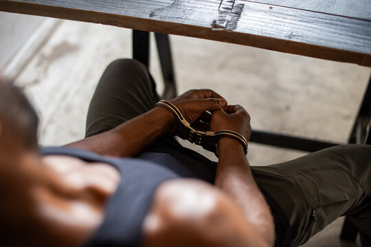 Person in handcuffs sitting at a table, wearing a dark tank top.