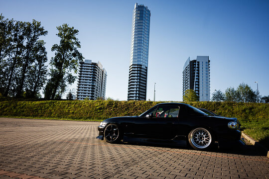 Black Mazda MX5 sports car parked beside modern high rise towers and city skyline in Katowice, Poland