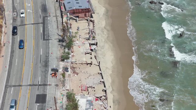 Top down aerial of Malibu beachfront real estate after demolition along Pacific Coast Highway with cars driving next to sandy Southern California shore