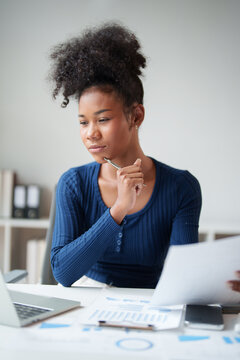 Young black businesswoman analyzing financial documents, thinking about strategy for business growth, making important decisions in a modern office setup