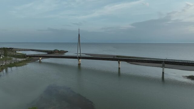 Horizontal drone aerial footage frame capturing the long wooden pedestrian bridge in Anaklia, showcasing the river delta meeting the Black Sea beach, a small green island, and coastal resort