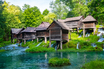 Fototapeta premium Scenic view of the historical Mlincici wooden watermills on Pliva River surrounded by small waterfalls and lush greenery in Jajce, Bosnia and Herzegovina
