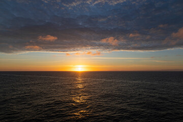Fototapeta premium Golden sunset over open ocean horizon with dramatic cloud layer and shimmering water reflections