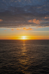 Obraz premium Golden sunset over calm ocean horizon with distant mountains and dramatic cloudy sky