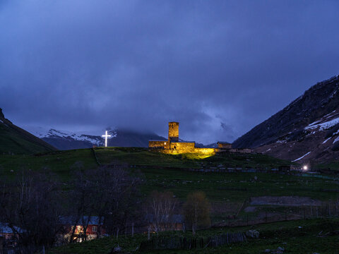 Horizontal landscape photograph capturing the historic Lamaria Church complex and medieval defensive stone tower on a green hill before nightfall, surrounded by misty mountains