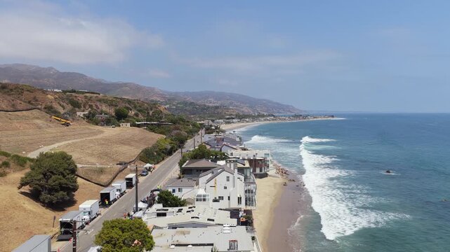 Aerial survey of prestigious Malibu real estate along Pacific Coast Highway showcasing luxury beachfront homes, sandy shores, ocean waves on a clear day in California