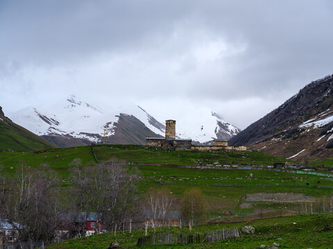 Horizontal landscape photograph capturing the historic Lamaria Church complex and medieval defensive stone tower on a green hill before nightfall, surrounded by misty mountains