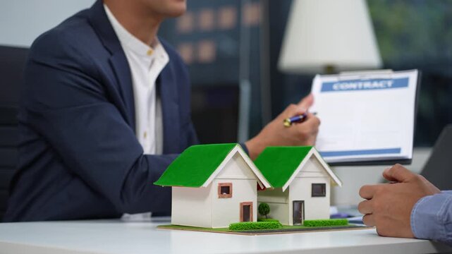 Real estate broker agent presenting and consult to customer to decision making sign insurance form agreement, home model, concerning mortgage loan offer in office.