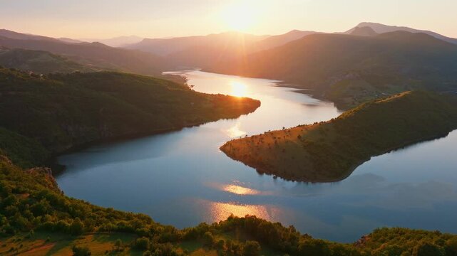 Cinematic Kardzhali reservoir meander curving through mountains valley sunset golden hour sun flare water surface sparkling aerial drone view travel Bulgaria