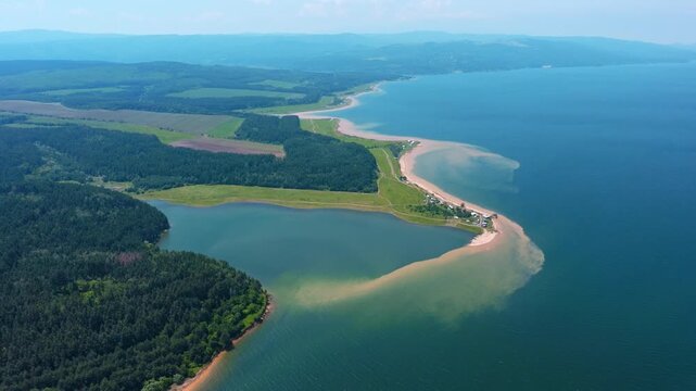 Sandy spit peninsula stretching out into deep blue water lake shoreline pine forest green meadows summer day aerial drone view Shiroka Polyana Bulgaria