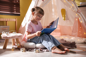 Little girl reading book in wigwam indoors © New Africa