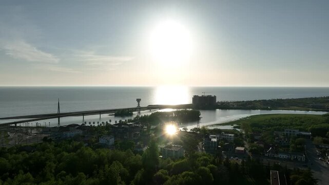 Horizontal drone aerial footage frame capturing the long wooden pedestrian bridge in Anaklia, showcasing the river delta meeting the Black Sea beach, a small green island, and coastal resort