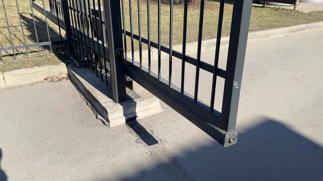 Automatic sliding iron gate, residential entrance, sunny spring day, closeup of lower track and wheel mechanism on asphalt