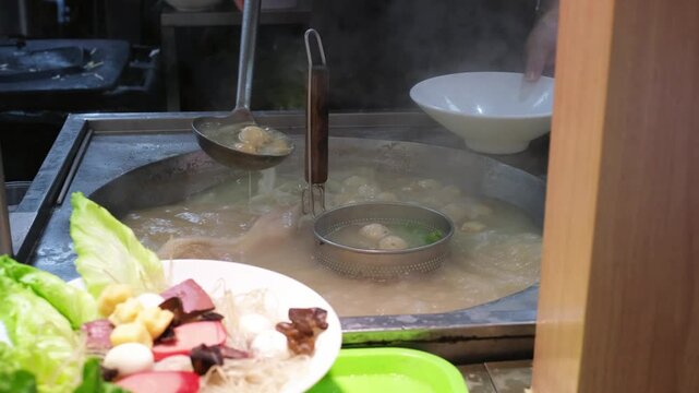 Chef blanching cabbage and mixing dumplings in boiling broth at street food stall. Traditional soup preparation and hawker center cooking technique, local culinary culture
