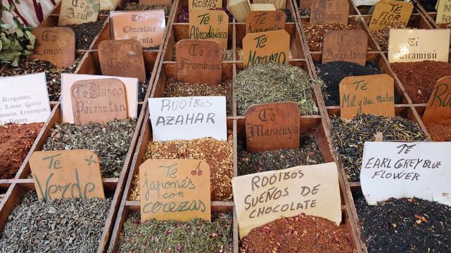 Traditional street market stall assortment of herbal teas in wooden boxes with handwritten Spanish labels aromatic spices ingredients close up