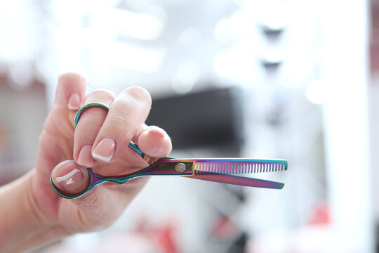Hairdresser holds scissors in his hand. Scissors for thinning. Close-up. Multi-colored metal scissors