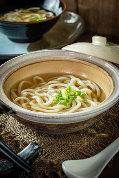Traditional Japanese kake udon noodle soup served hot in a ceramic bowl with savory dashi broth and chopped green onions. Minimalist authentic Asian comfort food. 