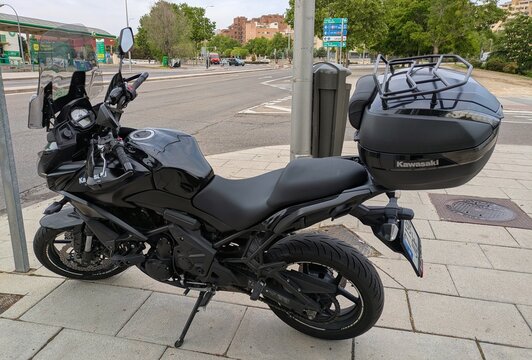 Vista lateral de moto Kawasaki Versys 650 con ba&uacute;l trasero original estacionada en Madrid, Espa&ntilde;a, 24 de abril de 2026