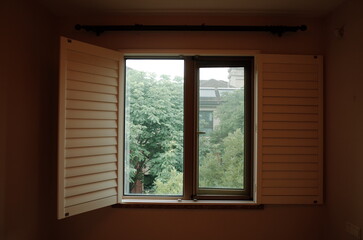 Fototapeta premium Open wooden shutters framing a view of green trees from an interior room