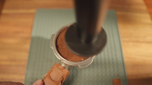 This POV footage shows a Baretta tamping freshly ground coffee in a coffee bottomless container to flatten the surface and then placing the filter on top, preparing it for the espresso machine.