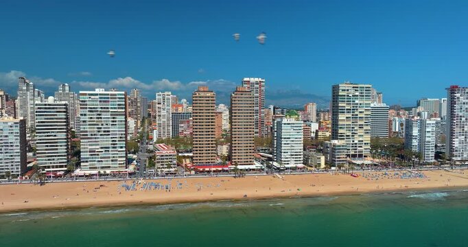 Benidorm beachfront skyline aerial view Spain Mediterranean summer high-rise buildings Levante beach tourists sandy shore turquoise water blue sky travel destination slow motion drone