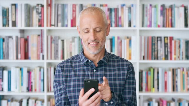 Teacher, mature and happy man with phone in library for academic study, knowledge or information. Male person, user or professor scrolling with smile on smartphone for online curriculum or syllabus