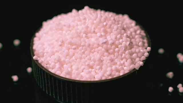 Pink micro beads in a small black container on dark surface