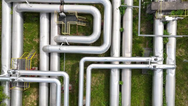 Aerial view of interconnected industrial pipes with green grass and walkways visible, showcasing the complex layout of a facility's piping system in an industrial setting