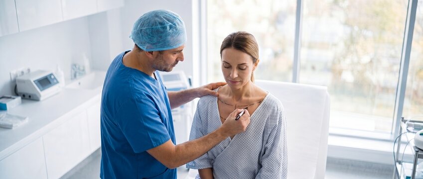 Plastic surgeon in blue gloves drawing preoperative markings on female chest for cosmetic surgery