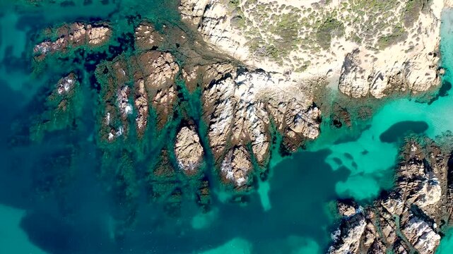 An Aerial top-down shot of rocky shoreline with turquoise waters and sandy patches along the coast