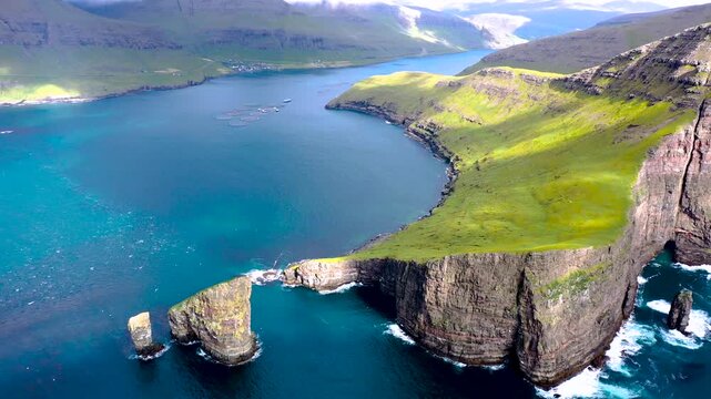 An aerial view of Drangarnir sea stacks rising from vivid blue waters between steep green cliffs in the Faroe Islands