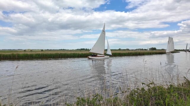 Elegant wooden sailing cruiser navigating the tranquil River Bure, surrounded by the scenic waterways and wildlife of the Norfolk Broads.
