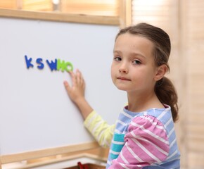 Naklejka premium Little girl learning alphabet with magnetic letters near whiteboard indoors