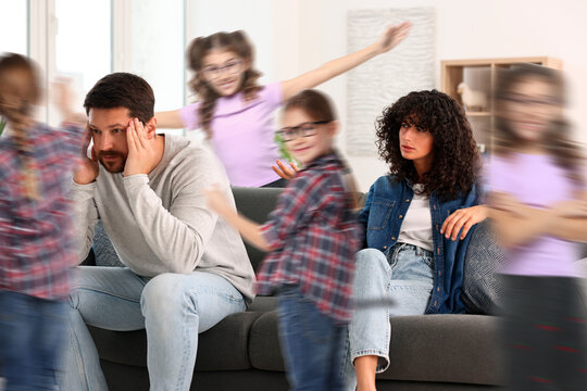Family with hyperactive children. Kids having fun while tired parents sitting on sofa