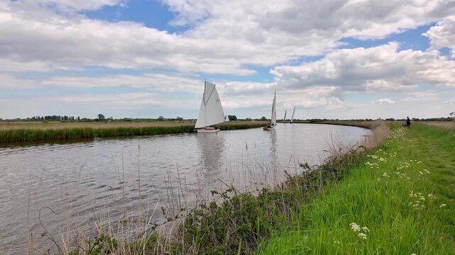 Traditional wooden sailing cruiser gliding along the River Bure on the Norfolk Broads, with calm waters, open skies and timeless English countryside.
