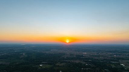 Fototapeta premium An aerial view of a vast rural landscape at sunset, with warm orange and golden hues fading into a calm blue sky above farmland and scattered villages. This image evokes serenity, openness