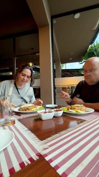 Vertical shot of a happy couple eating traditional Sri Lankan cabbage kottu roti with fried egg at an outdoor cafe, commercial lifestyle