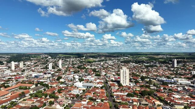 Aerial view of a sprawling city with terracotta roofs under a bright blue sky with fluffy white clouds